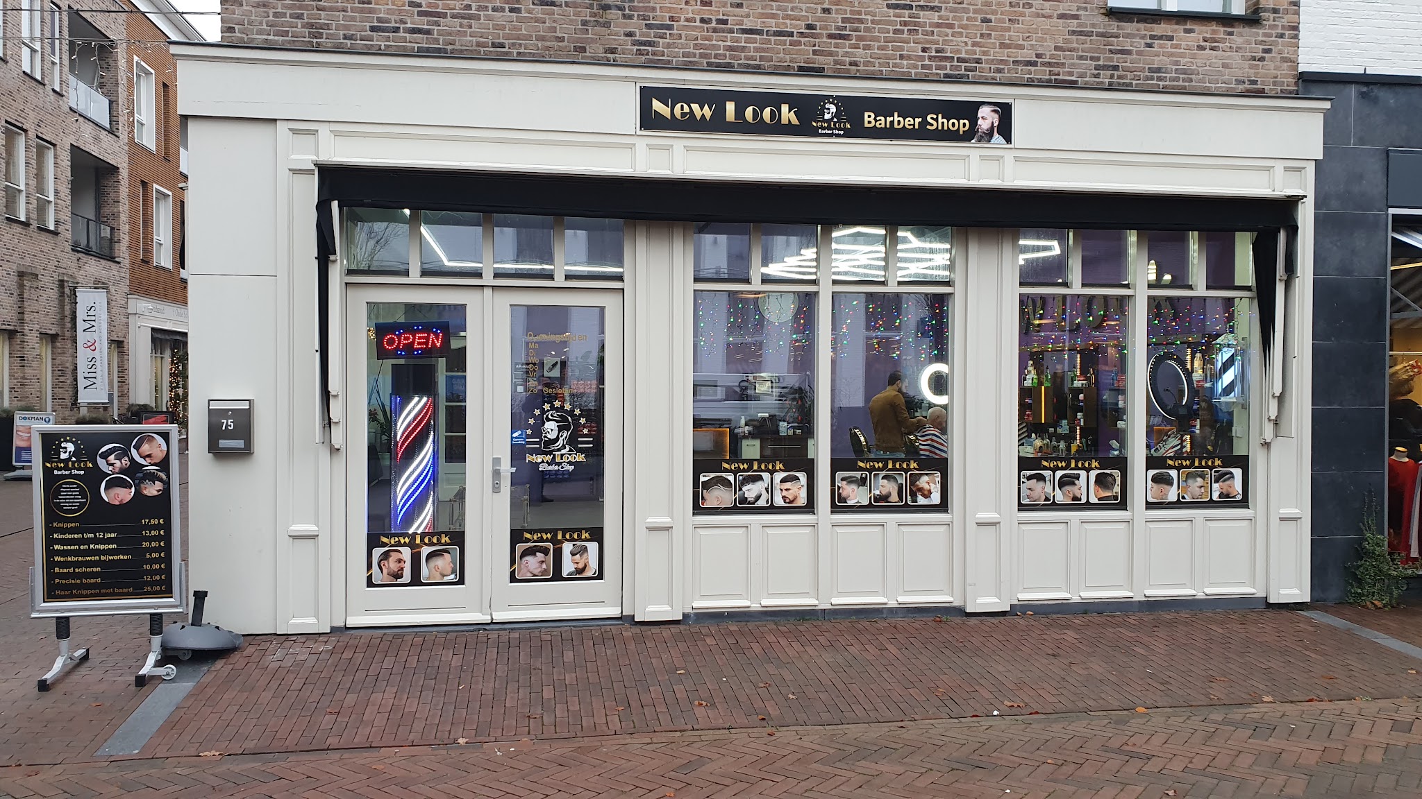 De winkelpui van New Look Barber Shop met het naambord, de kapperspaal en de zwart-gouden raamstickers